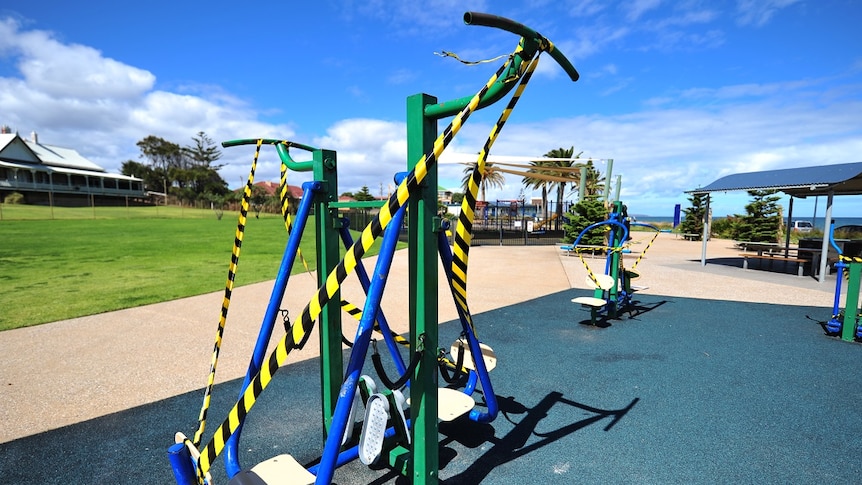 Outdoor public exercise equipment covered in yellow and black striped tape