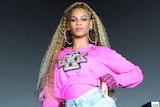 Beyonce stands at the top of a platform surrounded by male dancers in pink suits in a still from her Netflix documentary.