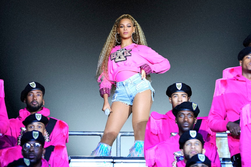 Beyonce stands at the top of a platform surrounded by male dancers in pink suits in a still from her Netflix documentary.