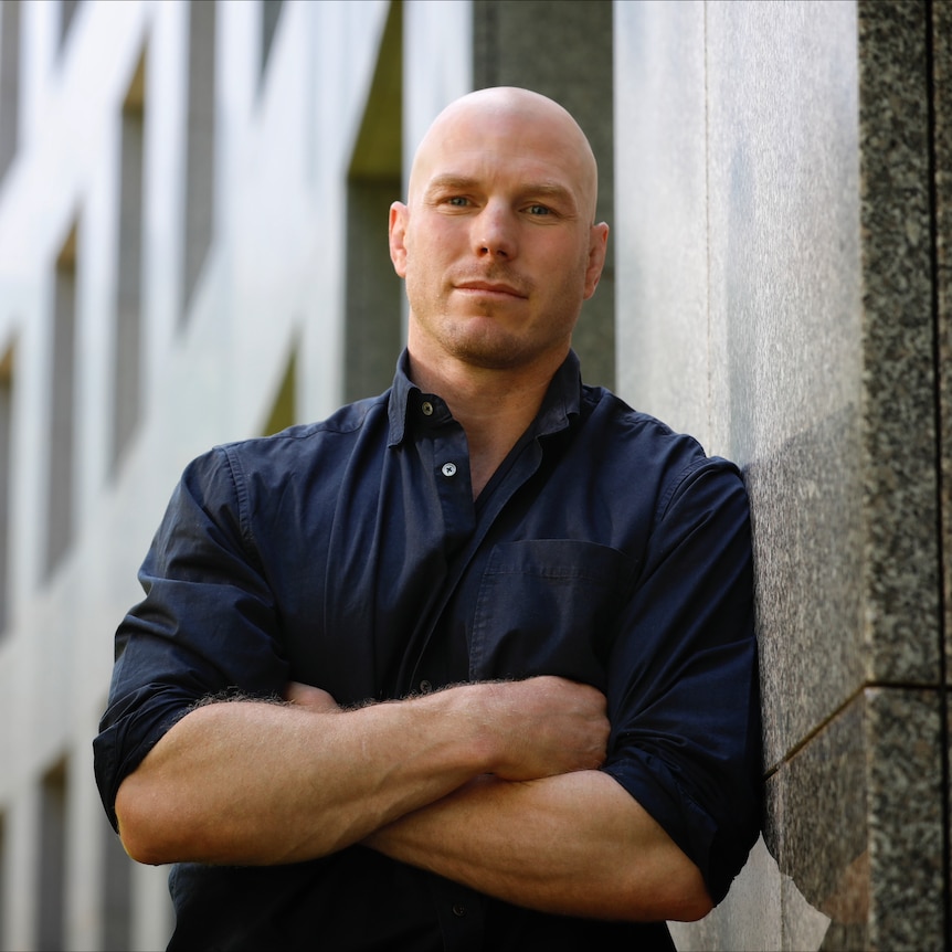 A man folds his arms and leans against a wall. 