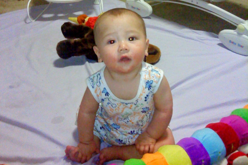 Baby Samuel Hill sits with his toys on a mat at home.