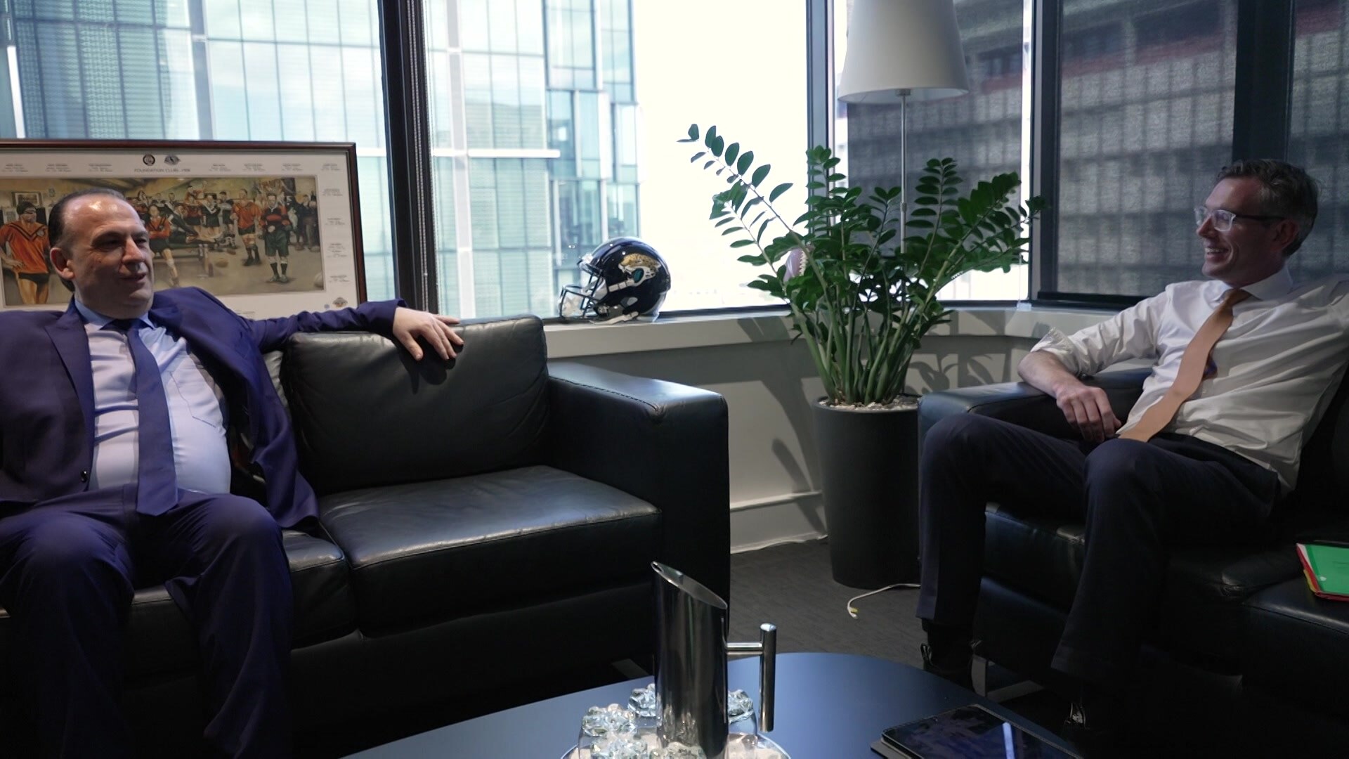 two men in business clothes sitting on opposite lounges