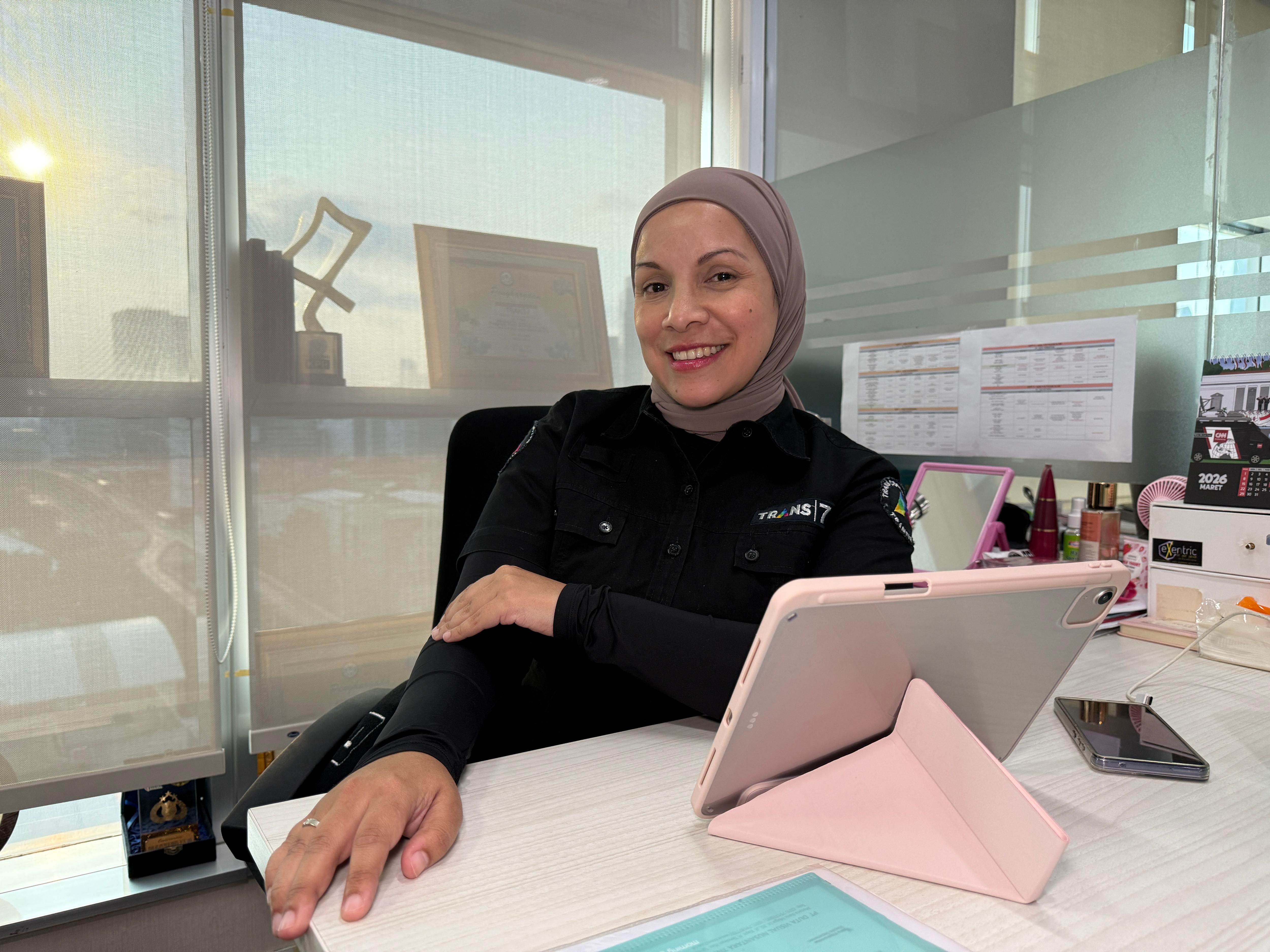 Woman wearing hijab sitting behind her desk smiling.