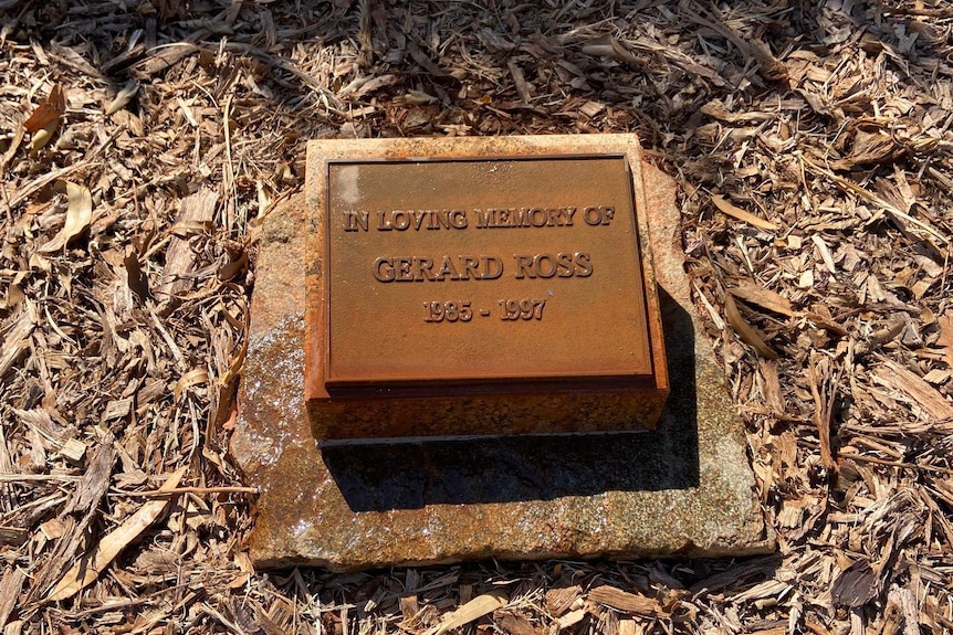 A small plaque memorial on the ground reading, 'In loving memory of Gerard Ross, 1985-1997'.