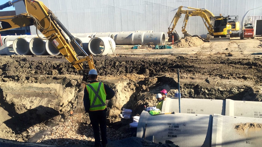 Workers and heavy machinery burying large concrete drainage pipes in Coffs Harbour CBD