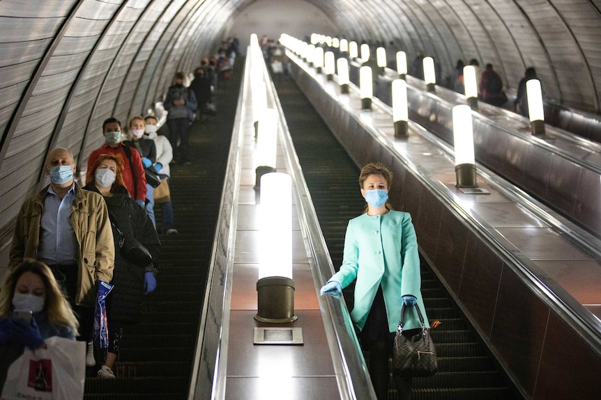 People stand in a line going down an escalator. they all wear masks