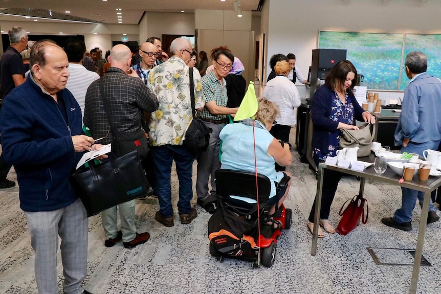 Shareholders stand around a table serving tea and coffee at an AGM