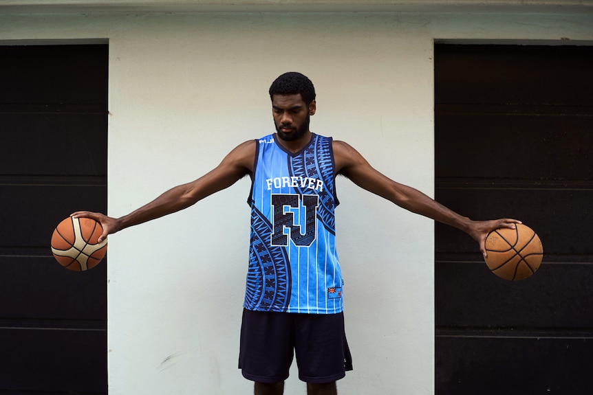 Buru with his arms outstretched holding a basketball in each hand