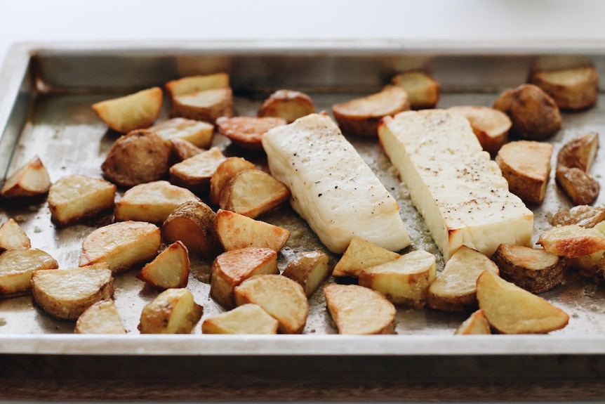 A tray of sliced potatoes with two slabs of halomi in the middle, two ingredients of a vegetarian tray bake.
