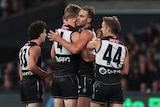 A Port Adelaide AFL player is hugged by a teammate (wearing #4) after kicking a goal.