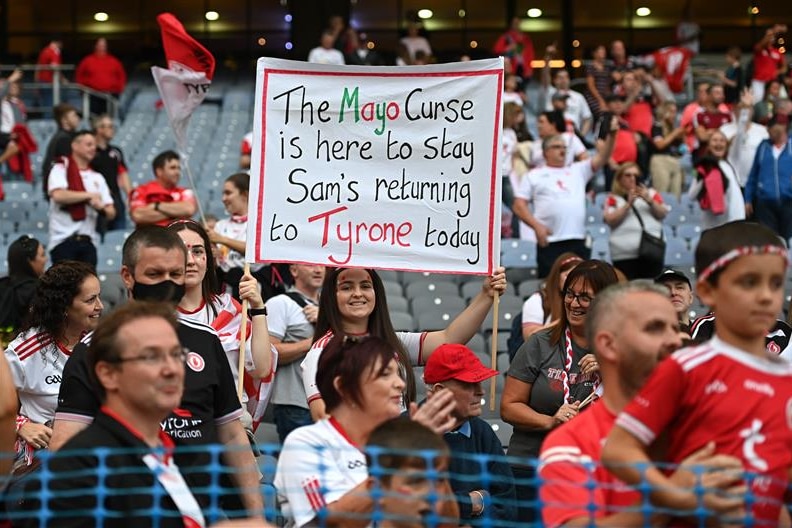 A Tyroine fan holds a banner saying "The Mayo curse is here to stay Sam's returning to Tyrone today".