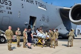 soldiers surrounding  a woman on a stretcher who is being taken off a plane