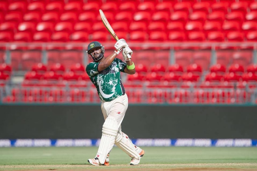 Suffan Hassan, wearing a green shift and white pants, plays cricket in a stadium 