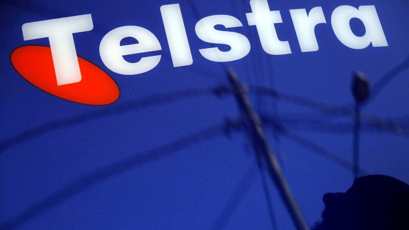 A man and power lines are reflected in a Telstra poster adorning a public telephone in Sydney