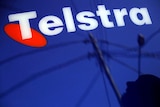 A man and power lines are reflected in a Telstra poster adorning a public telephone in Sydney