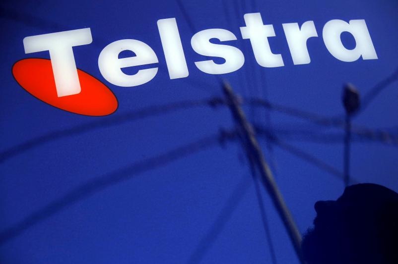 A man and power lines are reflected in a Telstra poster