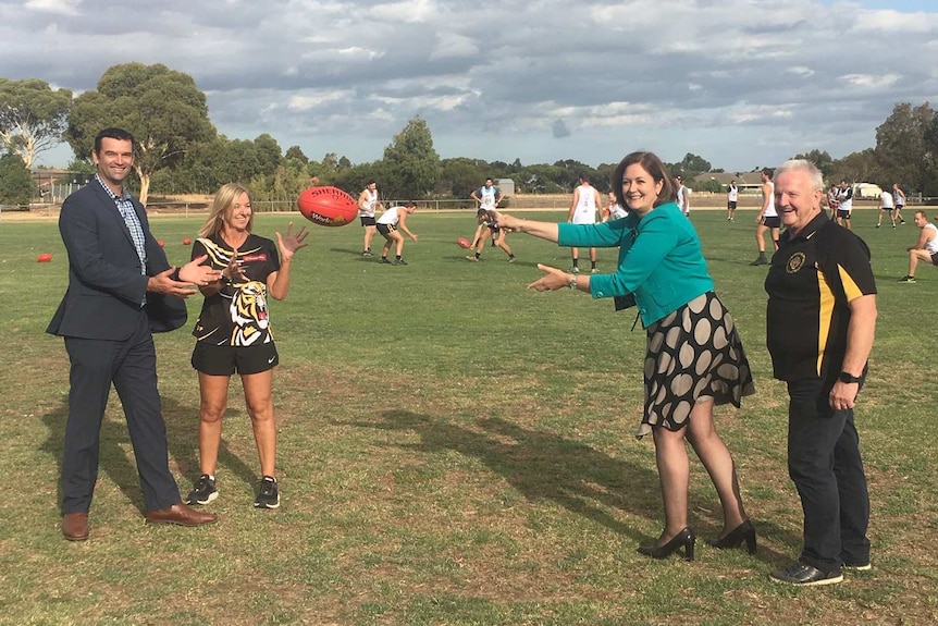 A woman with office clothes passes a football on an oval
