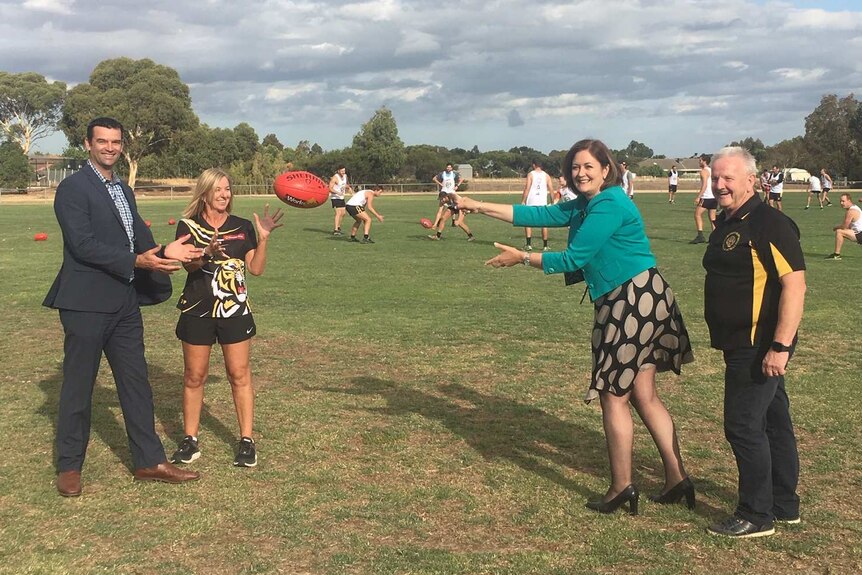 A woman with office clothes passes a football on an oval