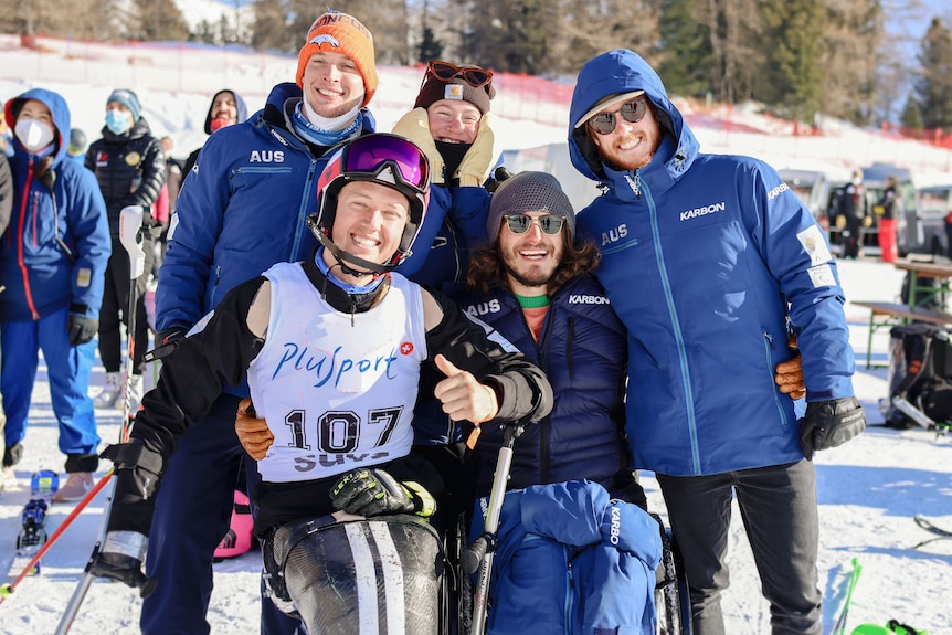 Para-athletes gather around Sam Tait who is in his sit-ski. 