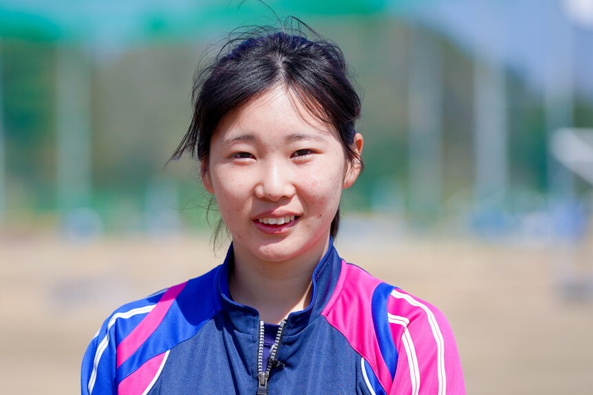 A young Japanese teen in a purple and pink athletic jacket 