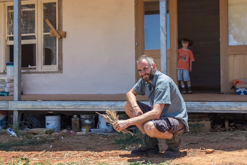 A man holding straw outside a partly constructed house