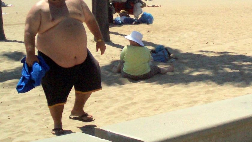 An obese man walks along a beach