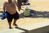 An obese man walks along a beach