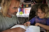 Father and daughter sitting around a small table in a campervan-style bus with a compass and an open book.