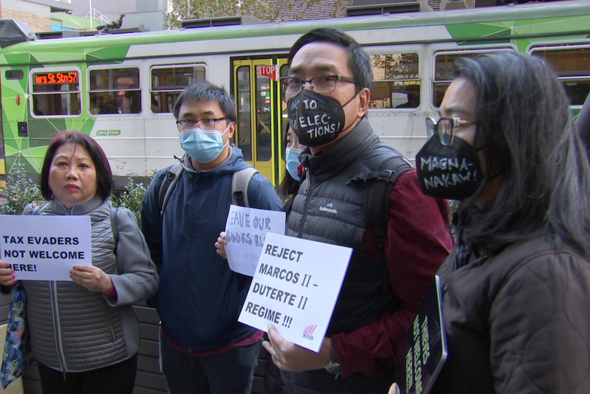 Protesters hold up signs with a tram in the background. 