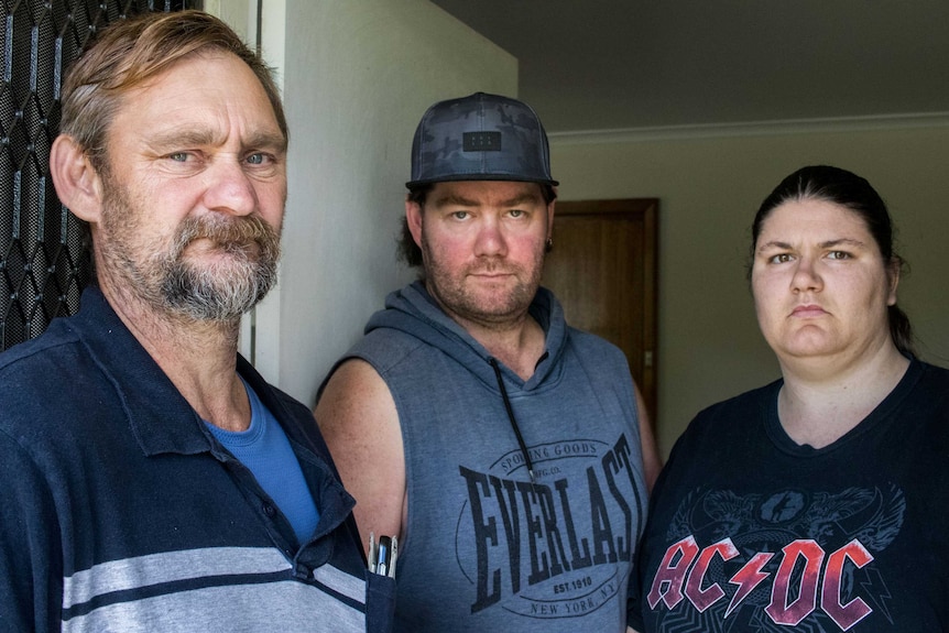 Three people pose in a doorway with serious expressions.