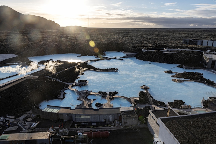 Boxy white buildings surround a blue lagoon with steam rising from it
