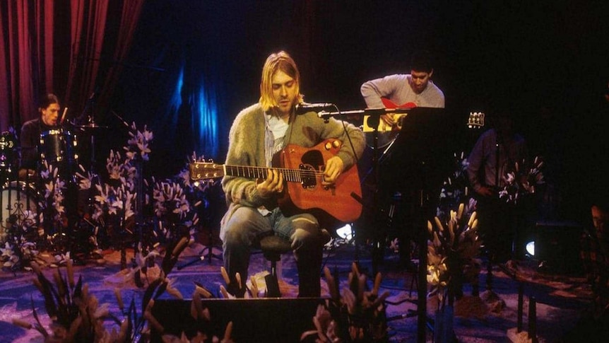 Kurt Cobain surrounded by flowers and playing his guitar at Nirvana's '93 MTV Unplugged performance