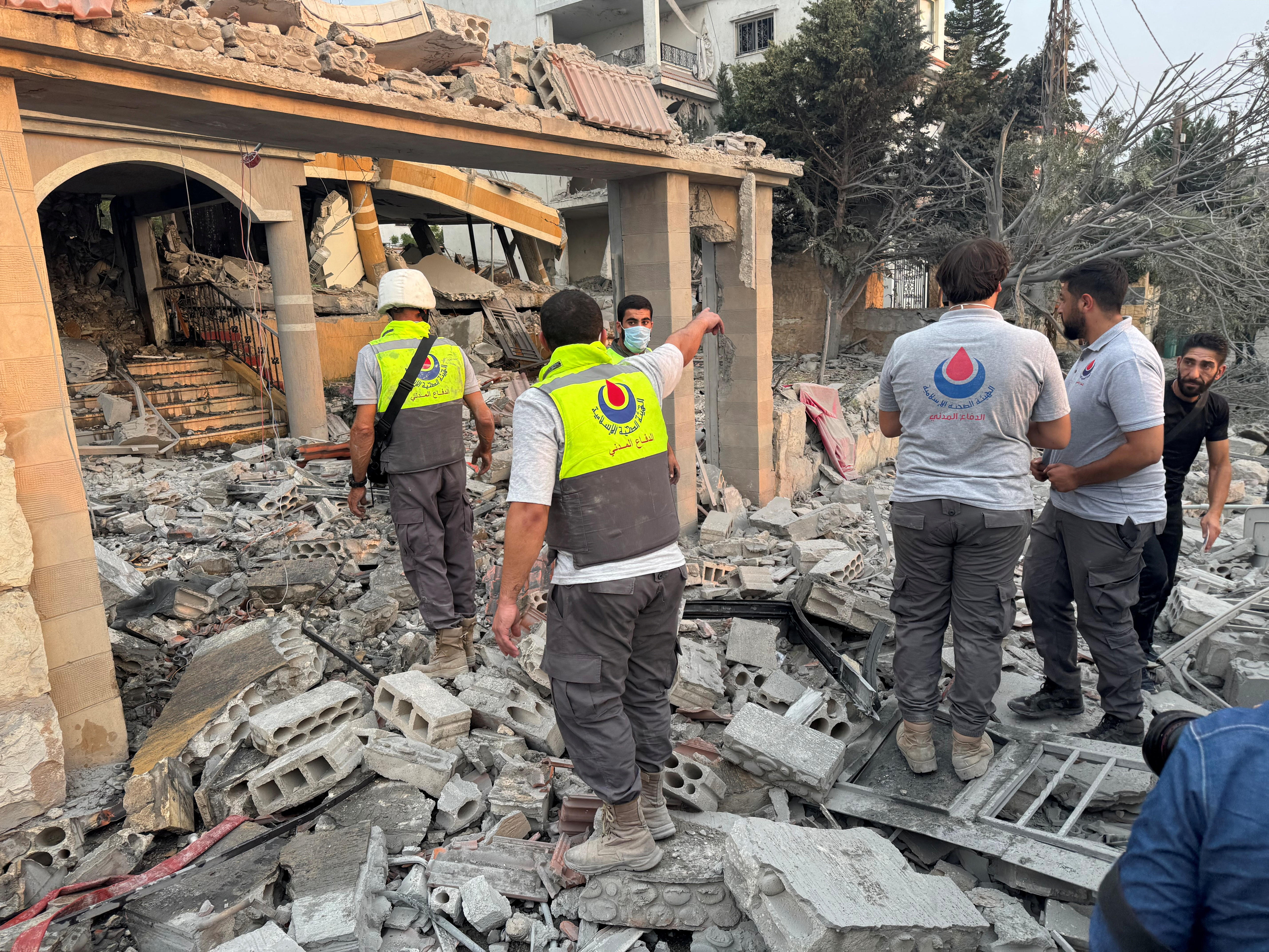 Men wearing high vis vests stand on rubble near a building