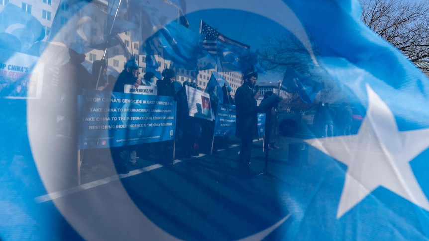 People protesting against against China's treatment of Uyghurs are seen reflected in a Uyghur flag.