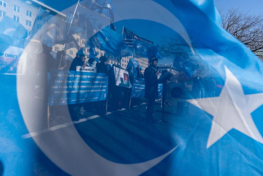 People protesting against against China's treatment of Uyghurs are seen reflected in a Uyghur flag.