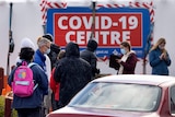 People line up in front of a 'COVID-19 Centre' sign
