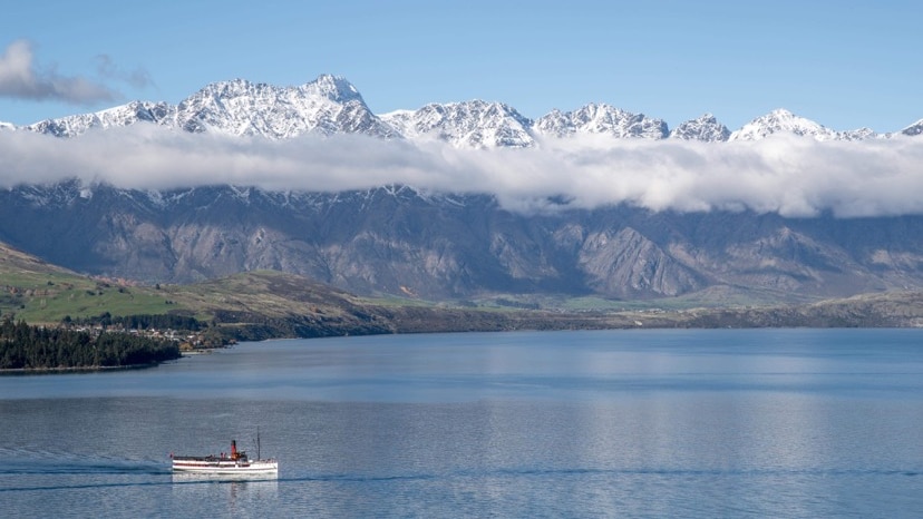 A boat crosses a lake with a mountain range in the background