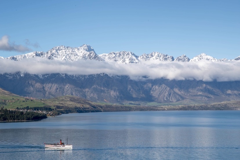 A boat crosses a lake with a mountain range in the background