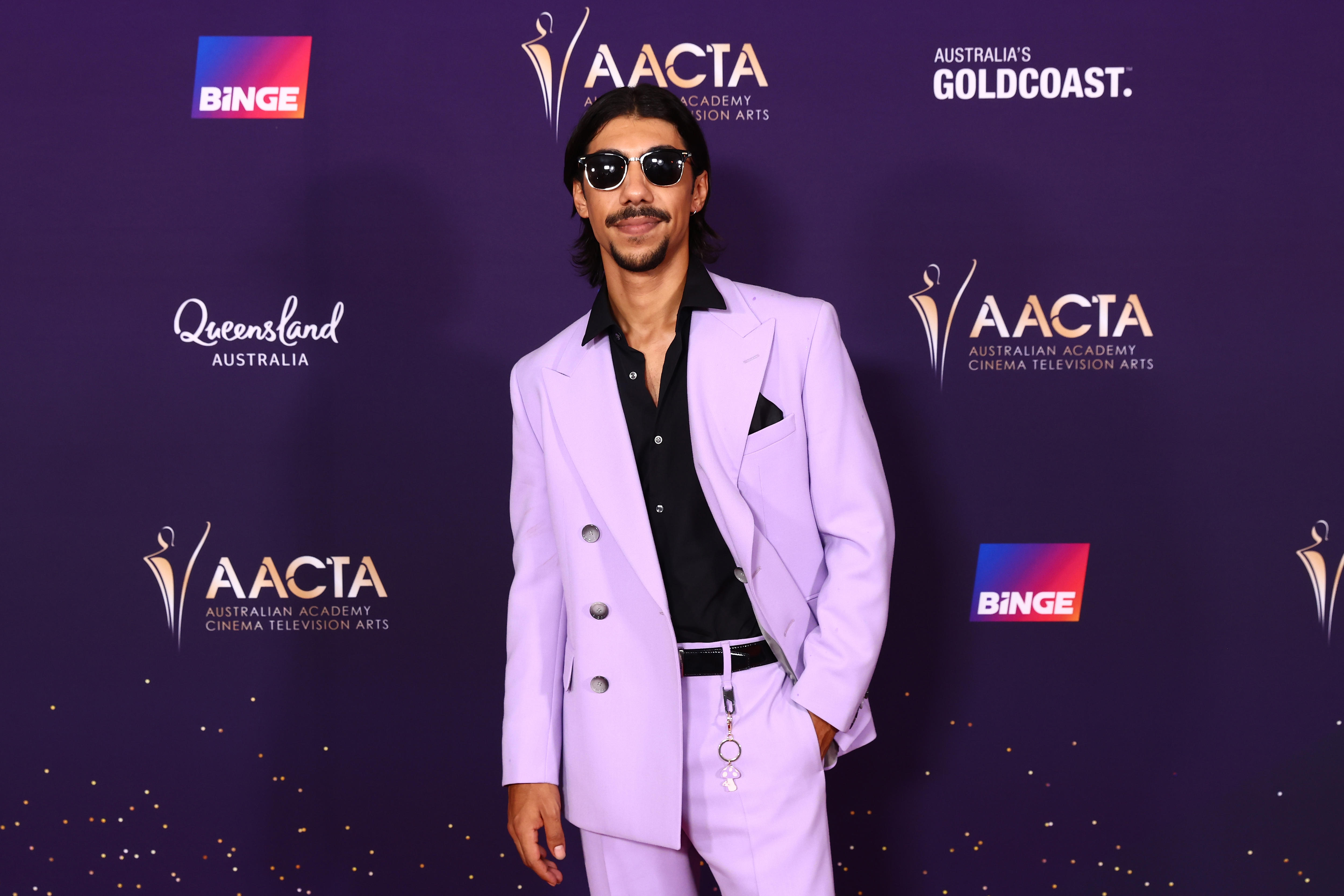 Hunter Page-Lochard wears a lilac suit with a black shirt, sunglasses and a little mushroom keyring on his belt