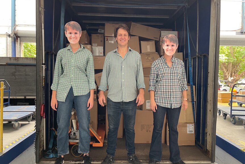 Man wearing green checked shirt standing at back of truck with two people dressed in same clothes, wearing masks of his face.