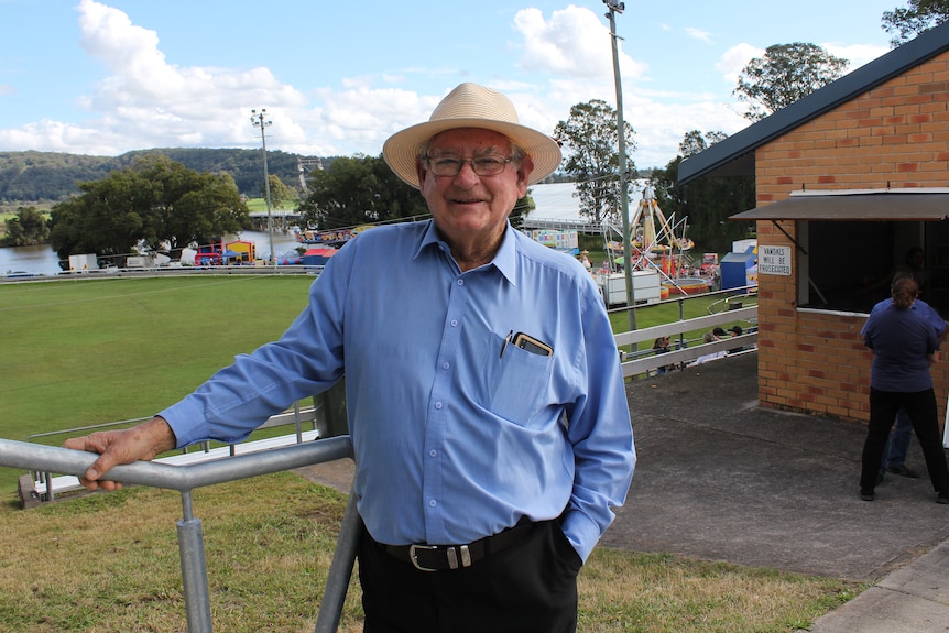 A man in a blue shirt and a cream hat stands holding a rail.