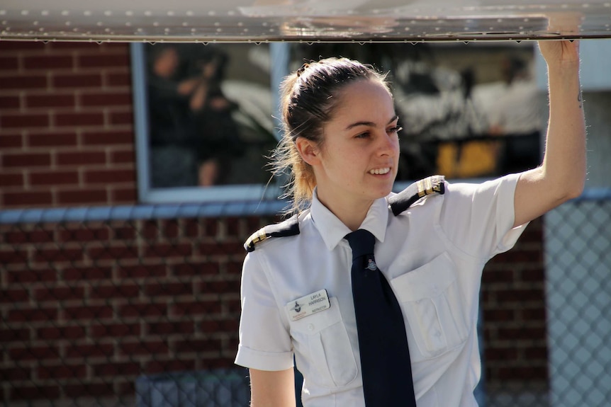 A female pilot under the wing of a light propeller aircraft.