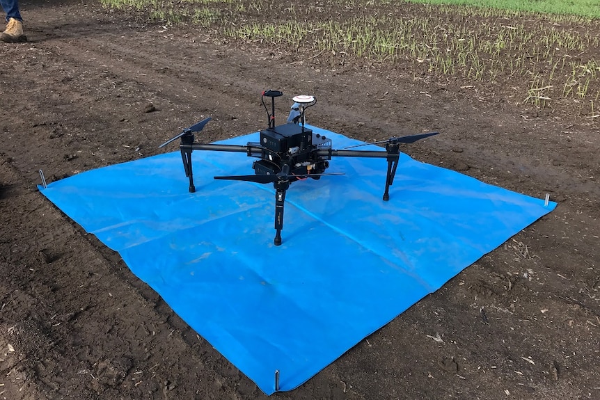 Large drone on blue sheet on the ground in field.