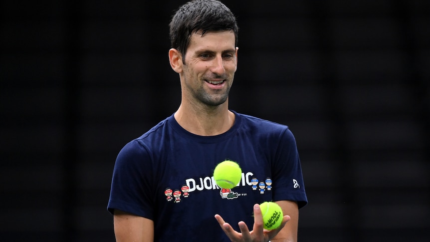 Novak Djokovic smiles and throws tennis balls in the air