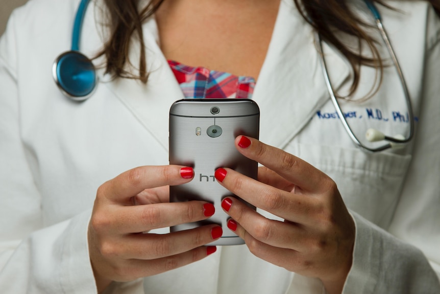 Female apparent doctor in white coat with stethascope with mobile phone in hand.