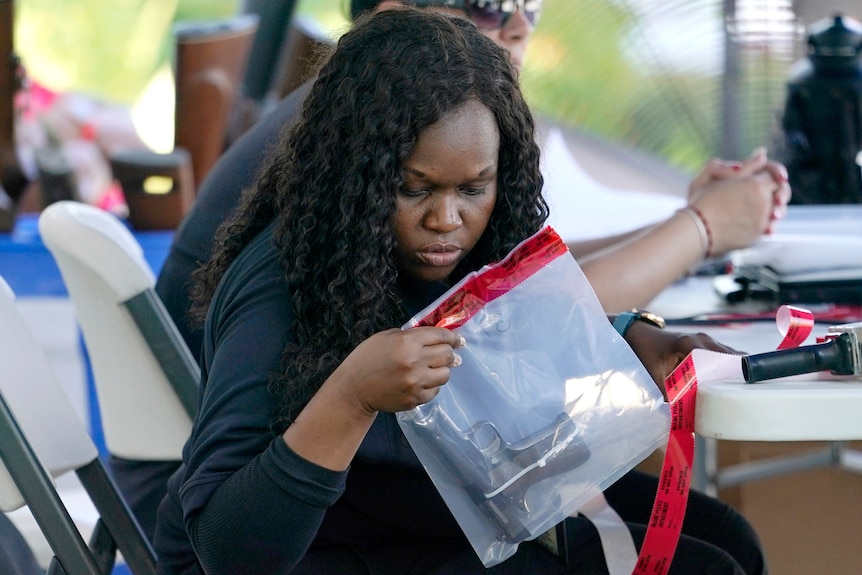 A black woman peers into a clear evidence bag, which contains a small black handgun