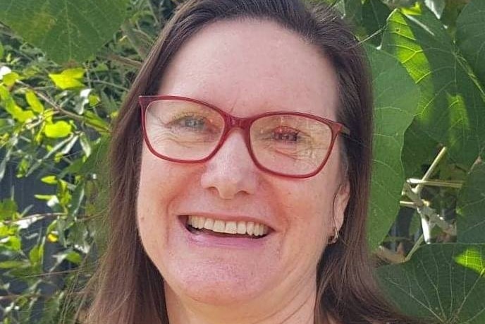 woman in red glasses stands in front of bushy tree