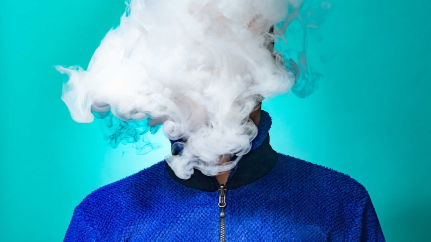 A masked man smoking vape and exhaling