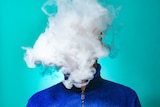 A masked man smoking vape and exhaling