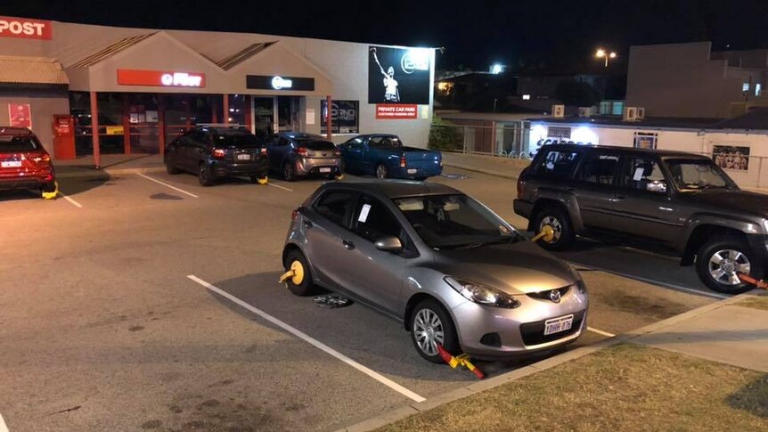 A car park showing several cars with wheel clamps attached.